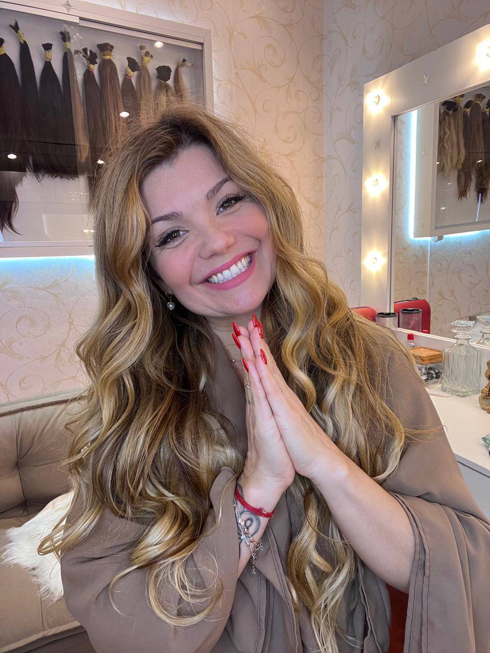 Fanny Martins sorrindo em seu estúdio de megahair, ao fundo mechas de cabelo humano organizadas